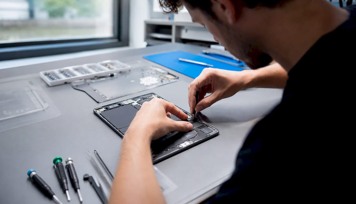 Een monteur is bezig met het repareren van een onderdeel van een tablet.