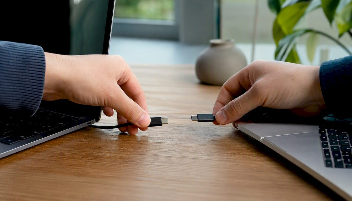 Twee handen sluiten een migratiekabel aan tussen twee laptops